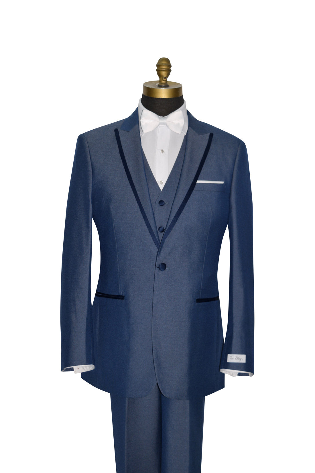 close-up Blue 3 piece peak lapel tuxedo with a white bowtie against a white background.