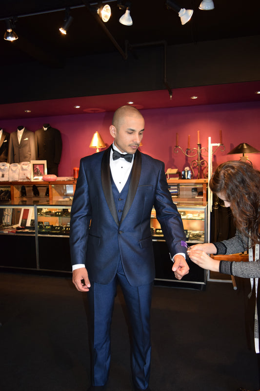 man wearing a blue tuxedo with a black shawl collar inside a tuxedo shop