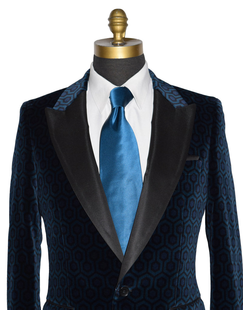 close-up mannequin wearing a blue hexagon velvet tuxedo jacket with a white tuxedo shirt and a long blue silk necktie against a white background