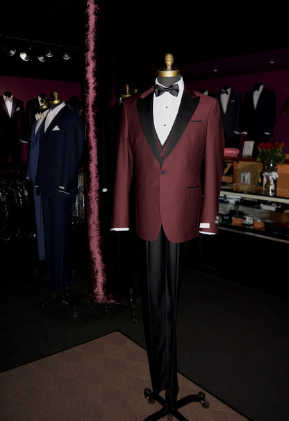 life-size mannequin wearing burgundy 3 piece tuxedo with black lapels in a men's store with tuxedos in the background