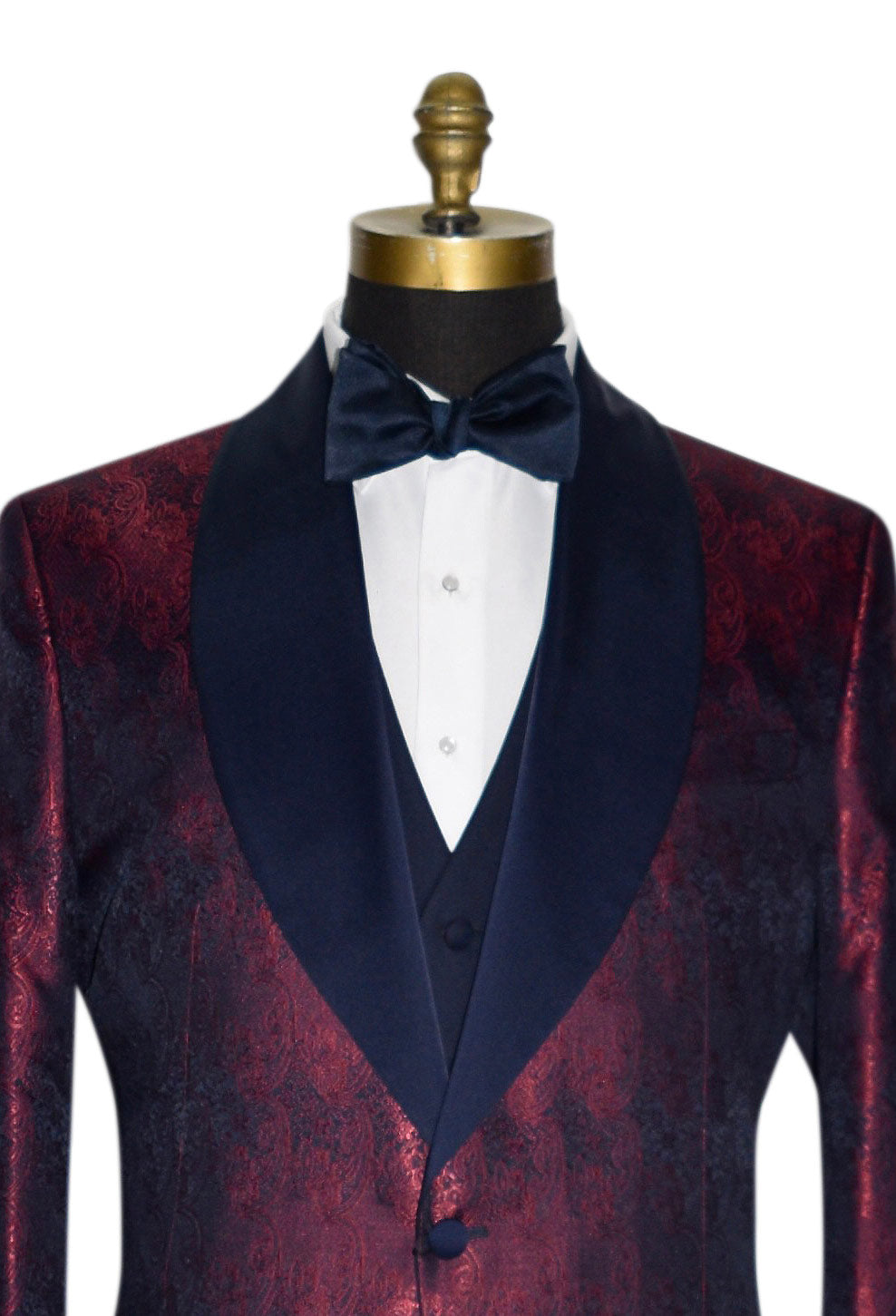 super close mannequin wearing a burgundy dinner jacket with navy blue lapel and navy blue paisley design with white tuxedo shirt against a white background