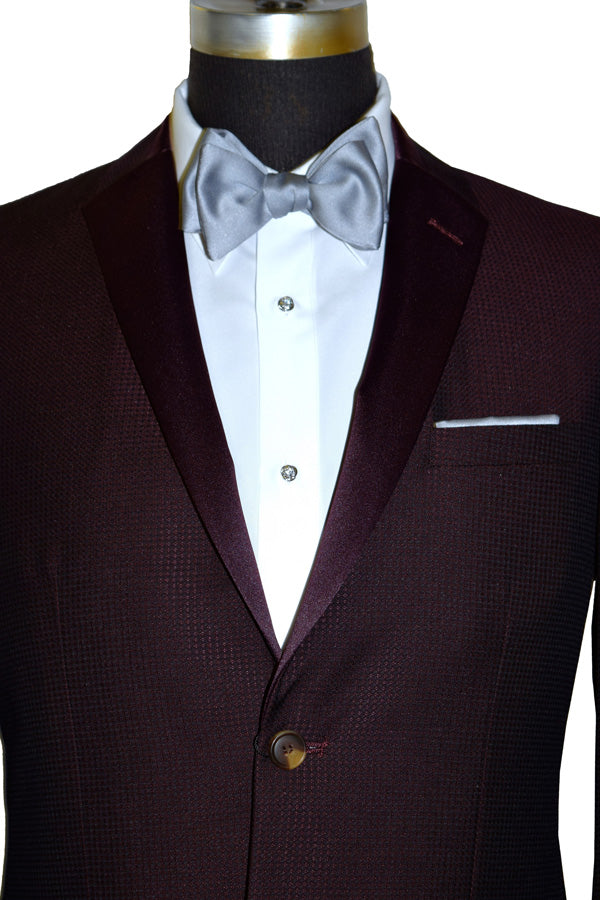 very close up burgundy tuxedo jacket with burgundy satin notch lapel with a gray bowtie and gray pants against a white background