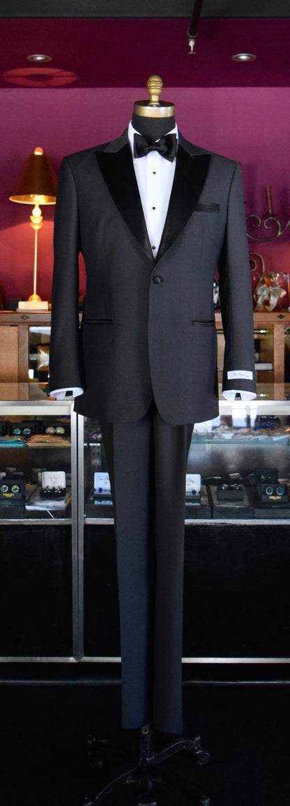 close up charcoal peak lapel tuxedo inside a mens tore against a purple wall