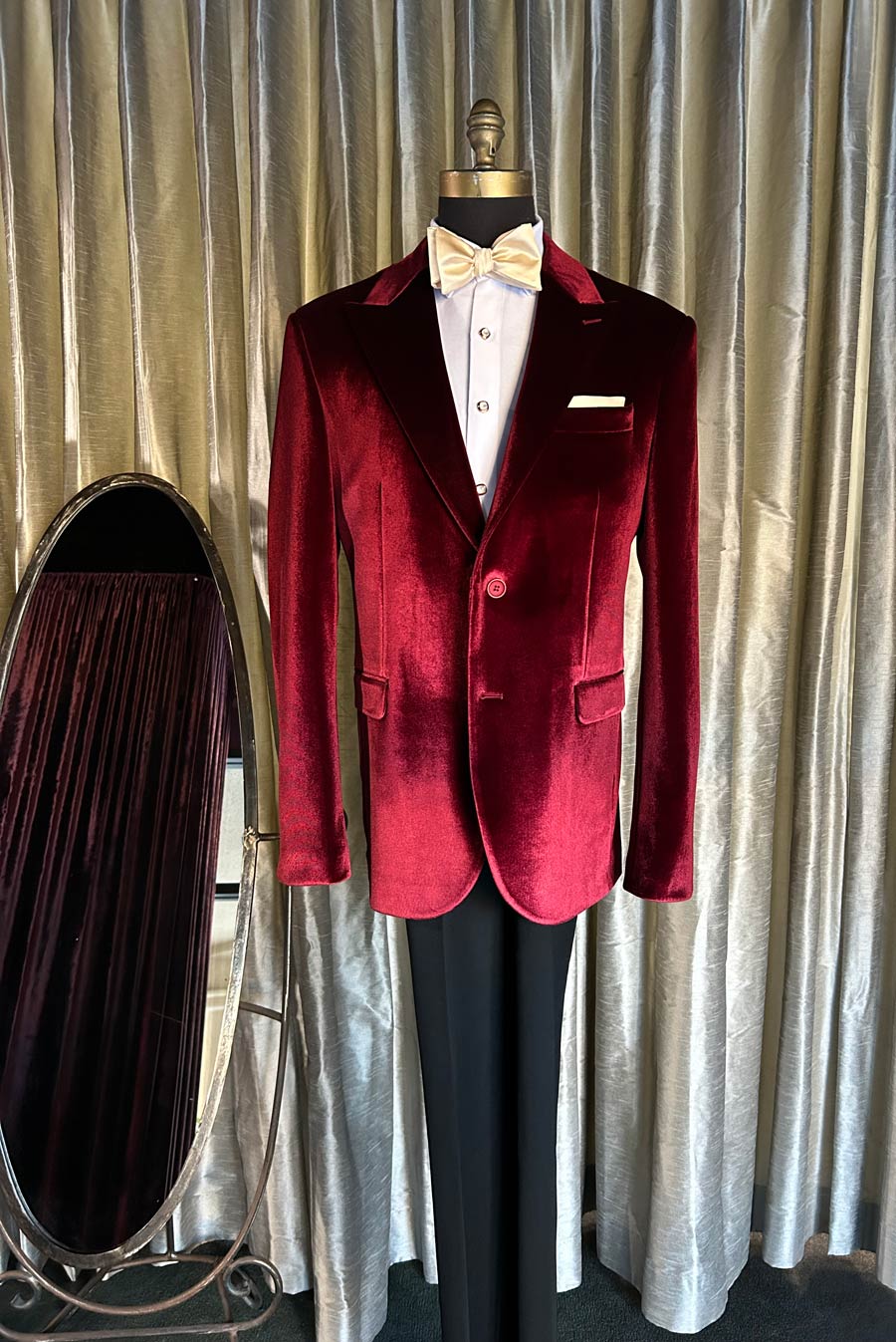full length mannequin wearing a velvet blazer with black tuxedo pants against a silver drape
