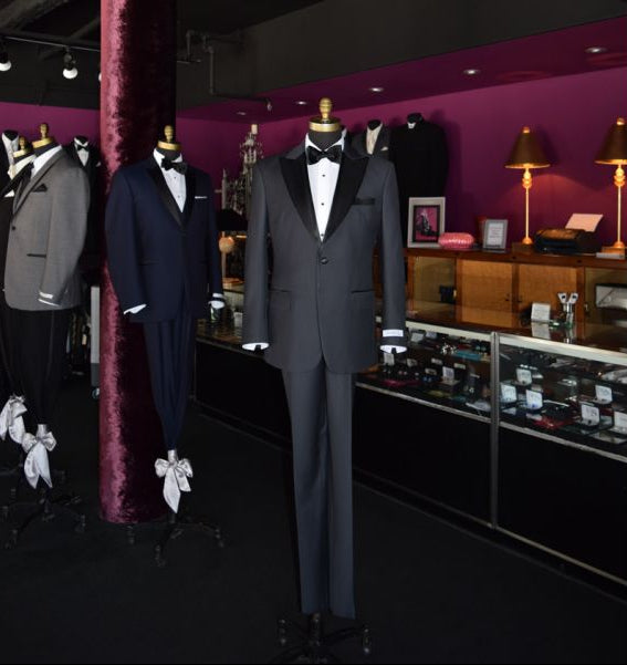 charcoal peak lapel tuxedo on display on a mannequin inside a tuxedo shop with other tuxedos on display in the background