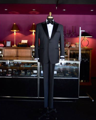 mannequin wearing a charcoal tuxedo inside a hi-end tuxedo shop with other tuxedos on display