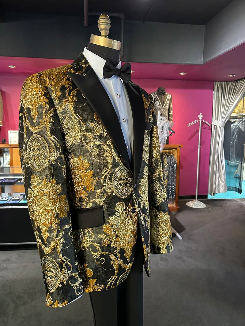 right side view close up of a mannequin wearing a gold and black brocade tuxedo with black peak lapels inside a tuxedo shop
