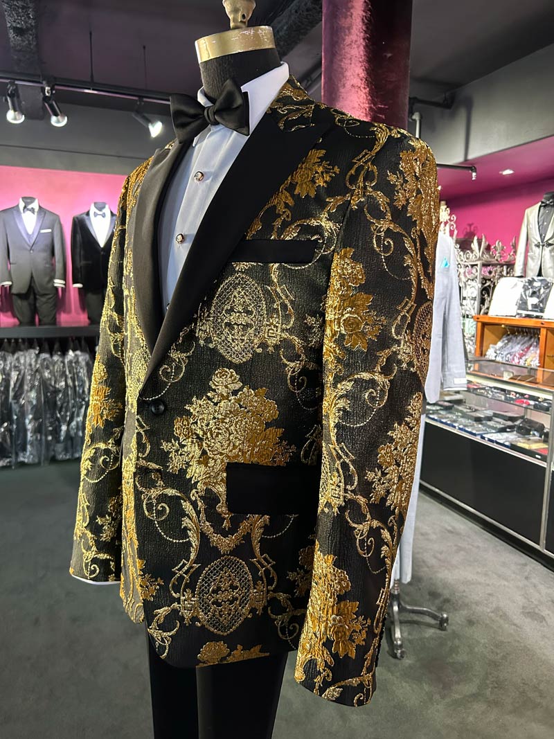 left side view of close up of a mannequin wearing a gold and black brocade tuxedo with black peak lapels inside a tuxedo shop