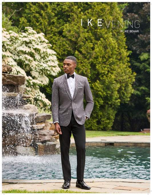 Man in a gray dinner jacket standing by a fountain with 'Ike Behar' branding.
