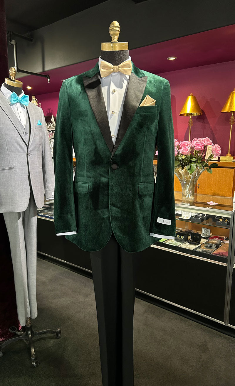 Full length mannequin wearing a green velvet tuxedo with black pants and a gold bowtie inside a tuxclub tuxedo shop