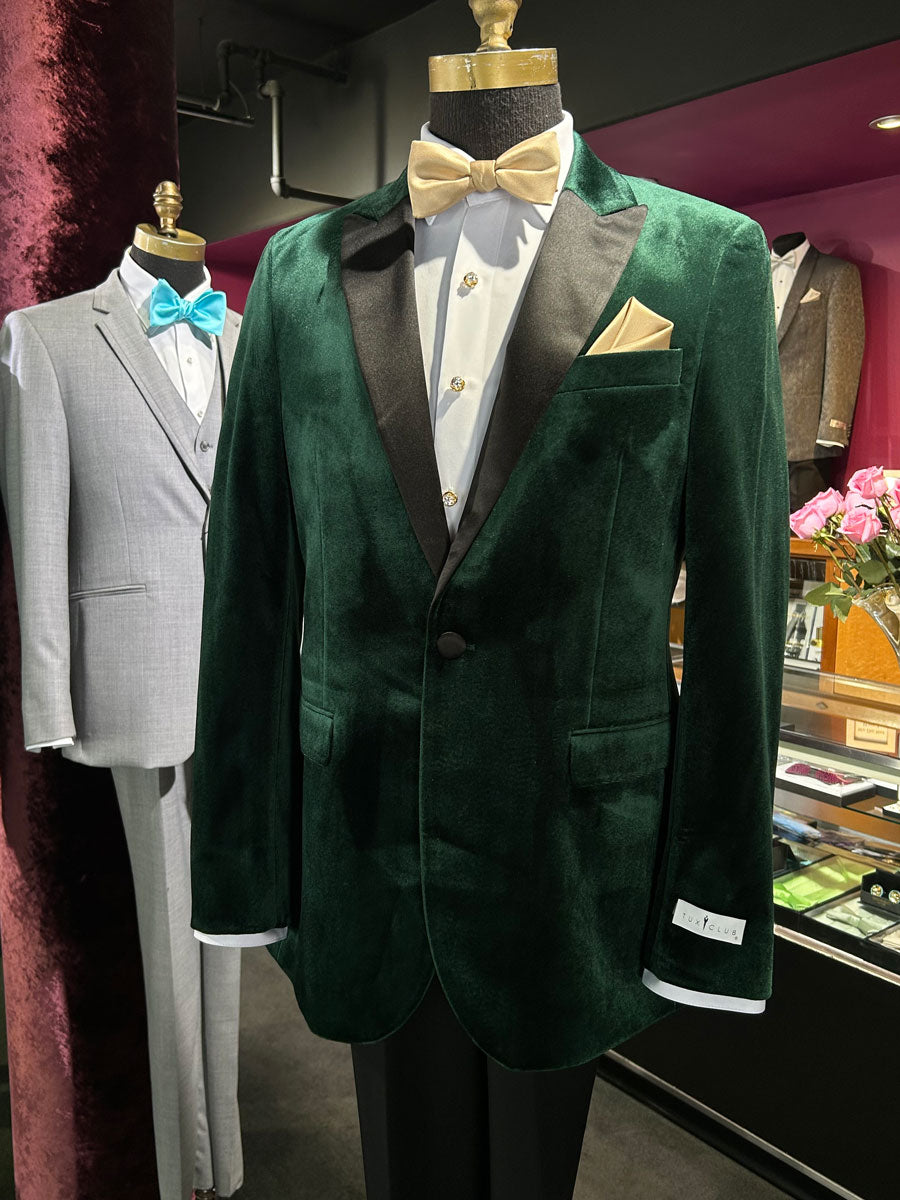 close up side view of a mannequin wearing a green velvet tuxedo with a white shirt and gold bow inside a tuxedo shop