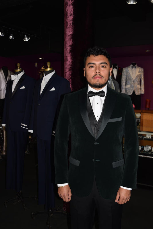 Man wearing a hunter-green velvet tuxedo in a fancy tuxedo shop standing in front of suits on mannequins