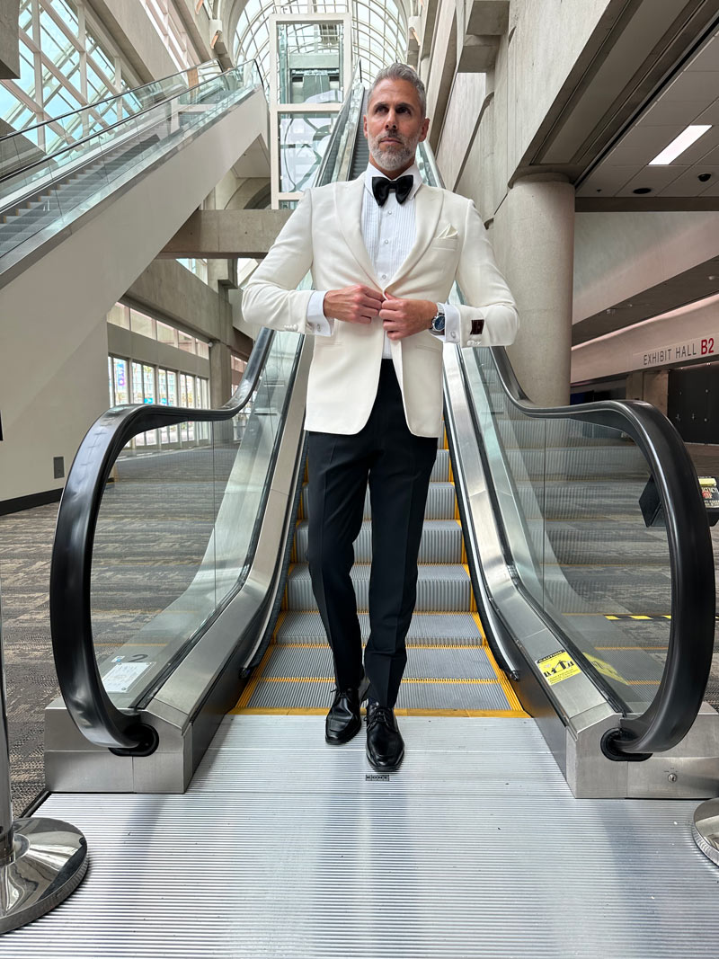 Man in a ivory peak lapel tuxedo tuxedo with white shirt and black bowtie while standing on an escalator