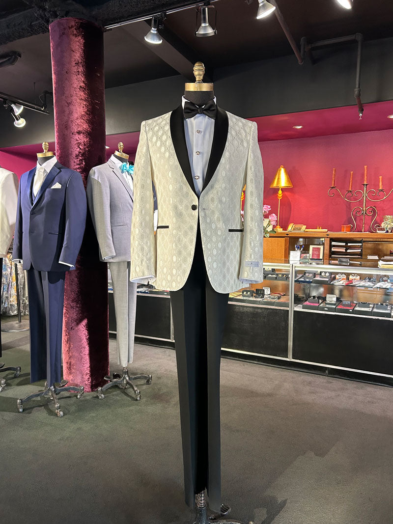 life size mannequin wearing an ivory shawl collar tuxedo with black lapel and black tuxedo pants in a fancy men's store