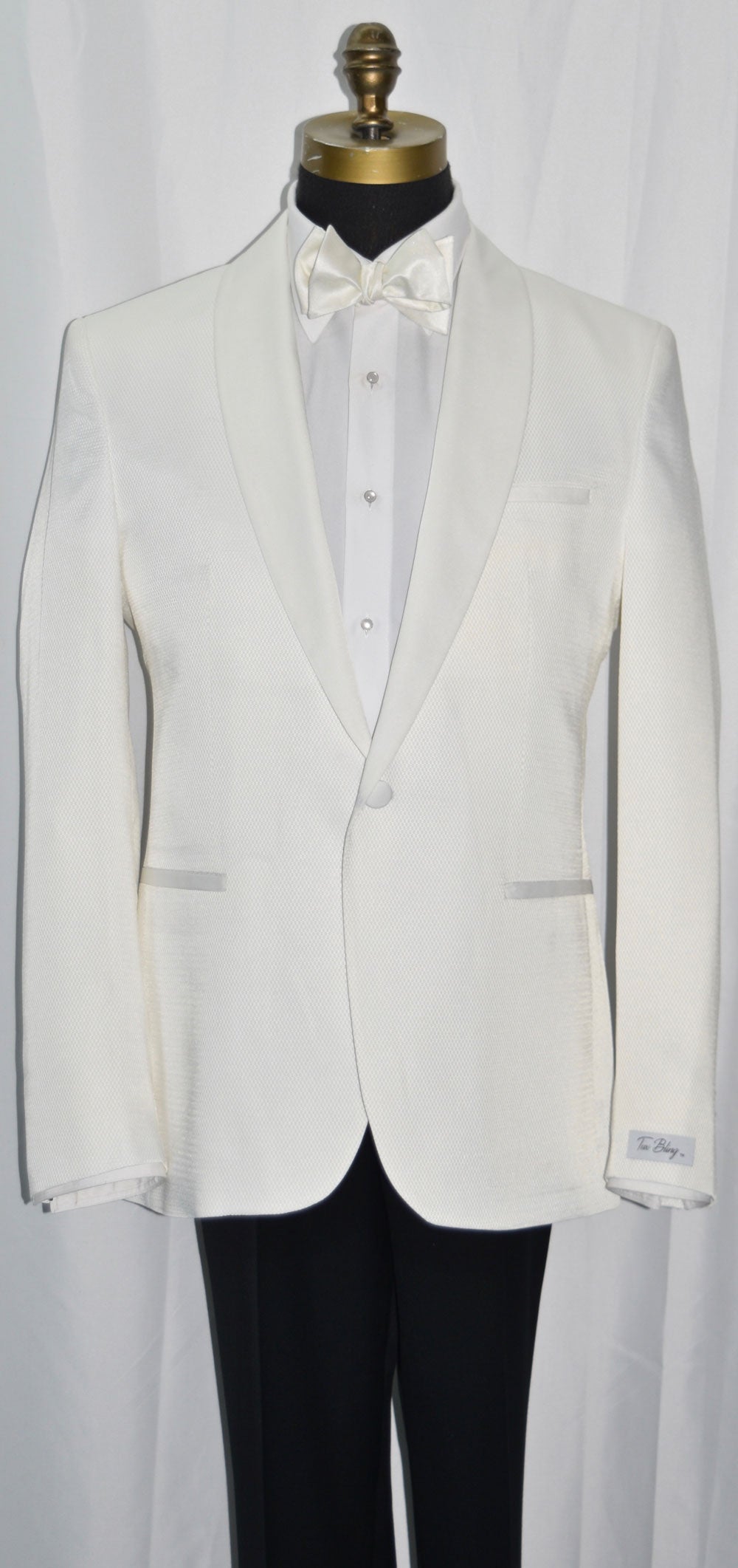 close-up life size mannequin mannequin wearing an ivory shawl collar tuxedo with a white tuxedo shirt and a ivory tie-yourself bowtie against a white background