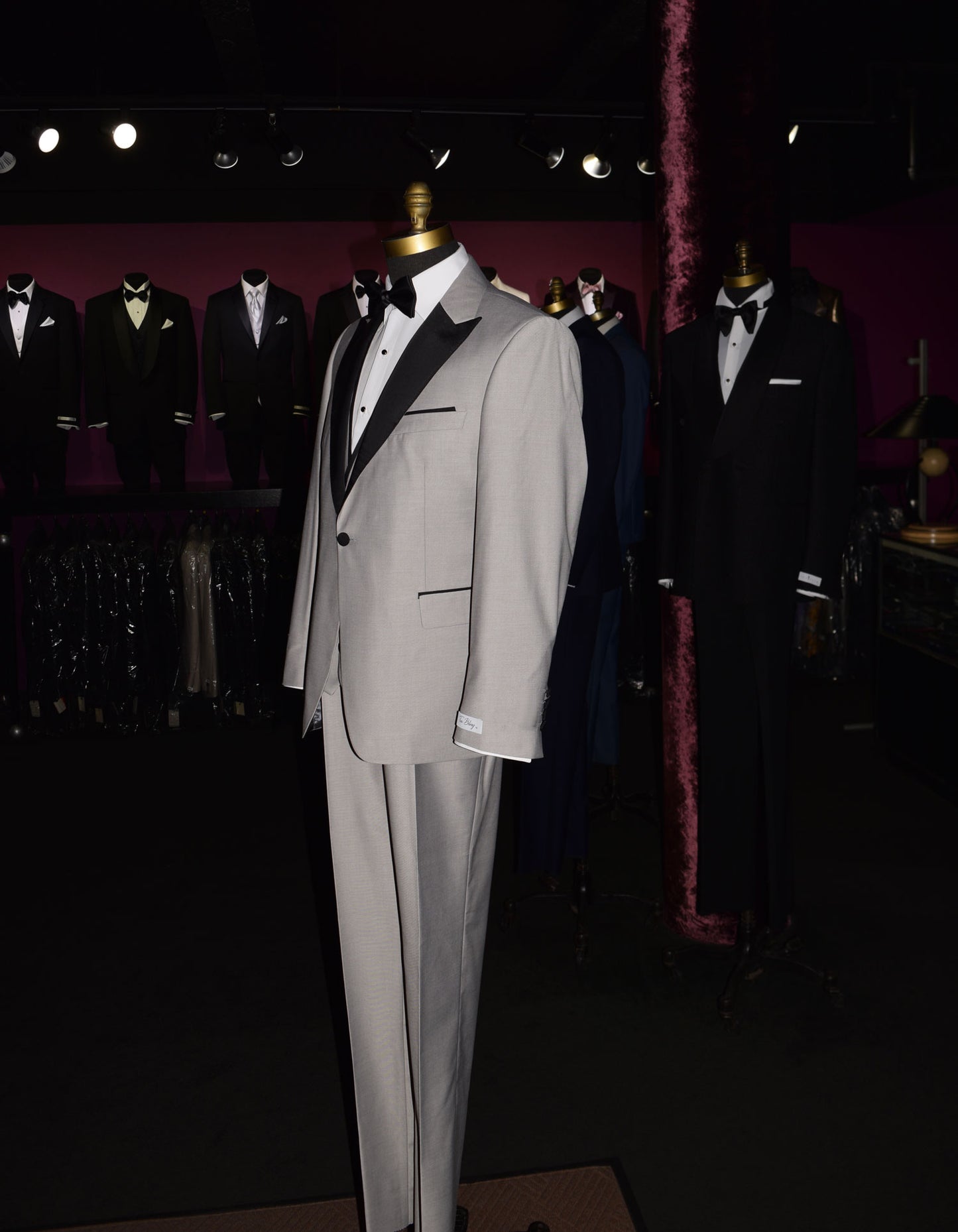 side view- life size mannequin wearing light gray peak lapel tuxedo with matching gray vest and black bow tie inside of a menswear shop