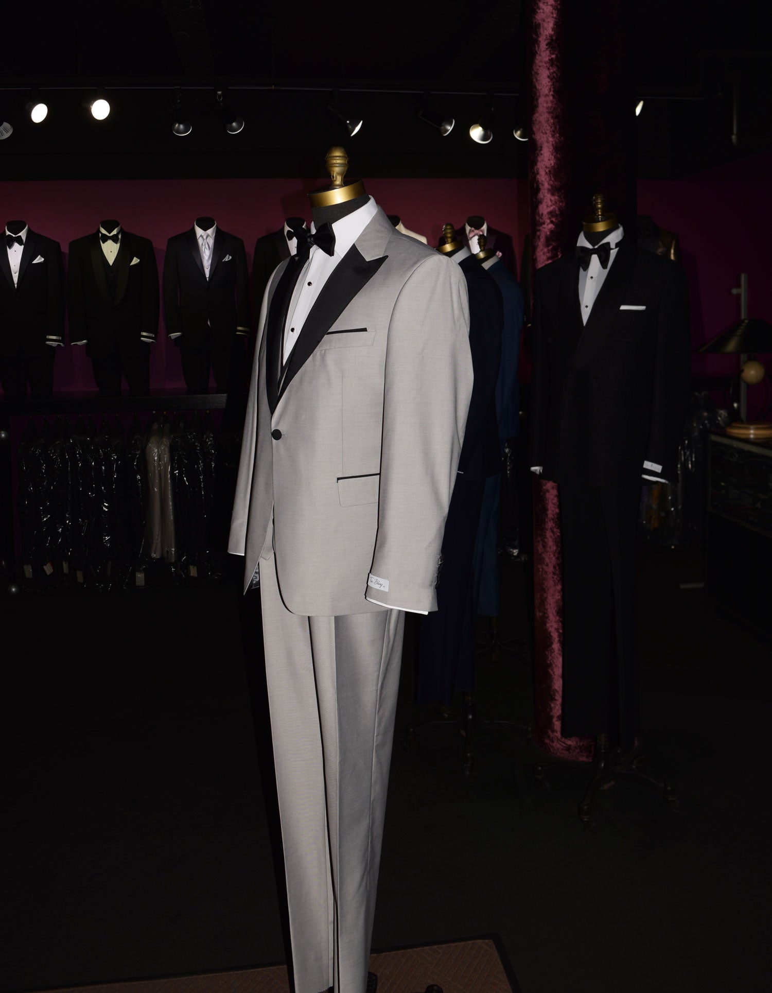side view- life size mannequin wearing light gray peak lapel tuxedo with matching gray vest and black bow tie inside of a menswear shop