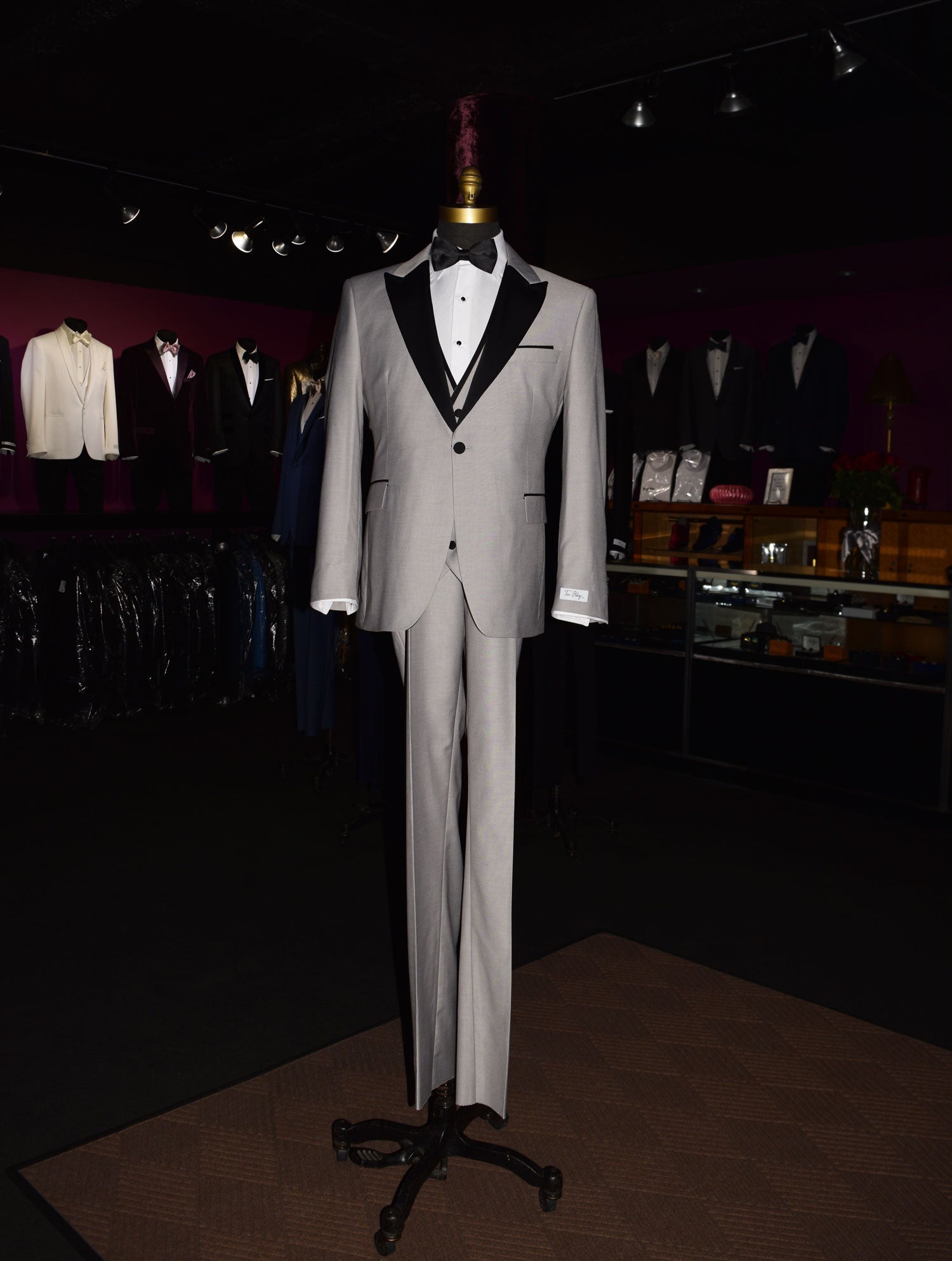 life size mannequin wearing light gray peak lapel tuxedo with matching gray vest and black bow tie inside of a menswear shop