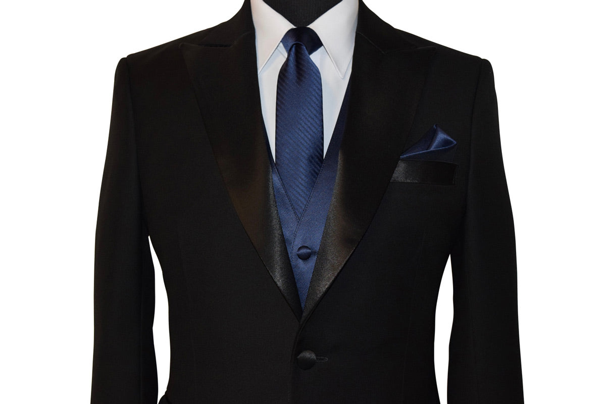 close-up black peak-lapel tuxedo wearing a white dress shirt with a marine blue striped necktie and a Marine blue tuxedo vest and pocket handkerchief against a white background  