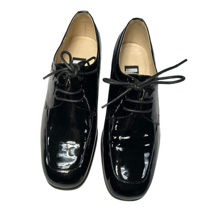 Pair of black patent leather shoes with laces on a white background