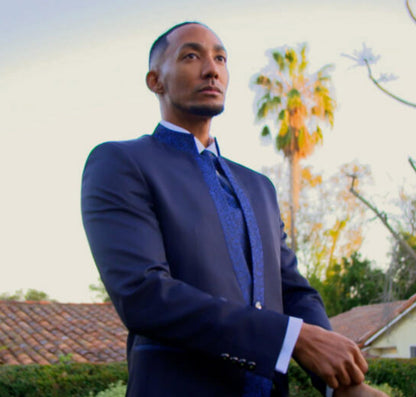 Man in a blue nehru collar tuxedo standing outdoors with palm trees in the background