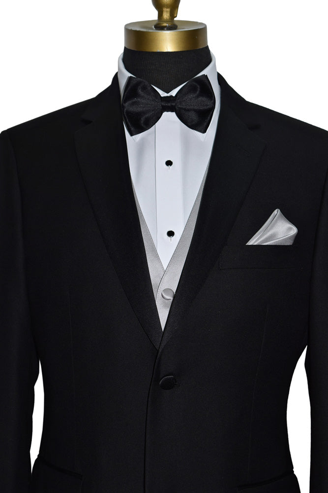 close-up Black notch-lapel tuxedo with white dress shirt and moonlight-vest with a black "pre-tied" bow tie and pocket handkerchief on a mannequin against a white background