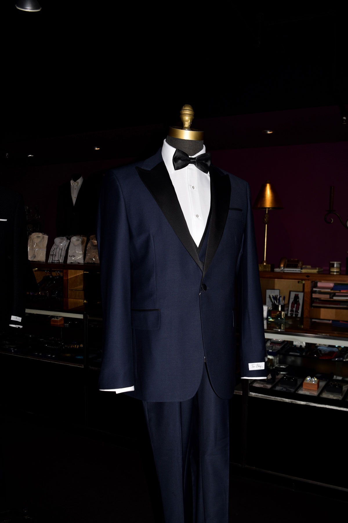 side view-close up mannequin Navy blue tuxedo with black lapels on a mannequin wearing a black bow tie inside of a fine mens store