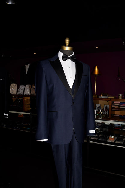 side view-close up mannequin Navy blue tuxedo with black lapels on a mannequin wearing a black bow tie inside of a fine mens store