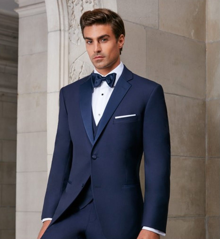Man wearing a navy-blue tuxedo with blue satin notch lapel with a navy-bow tie in an elegant setting