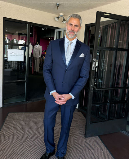 Man in a navy blue tuxedo standing in a tuxedo shop with mannequins in the background