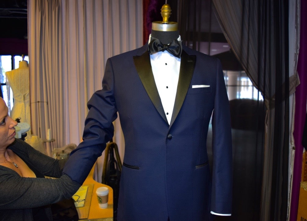 sales lady dressing a mannequin with a navy blue tuxedo inside a tuxedo shop