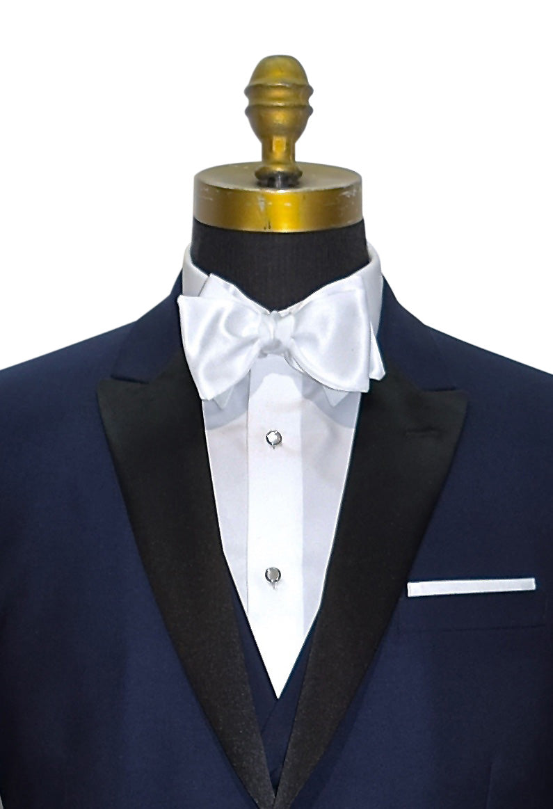 very close front view mannequin wearing a navy blue tuxedo with black peal lapels with matching navy tuxedo pants with white shirt and white satin bowtie against a white background