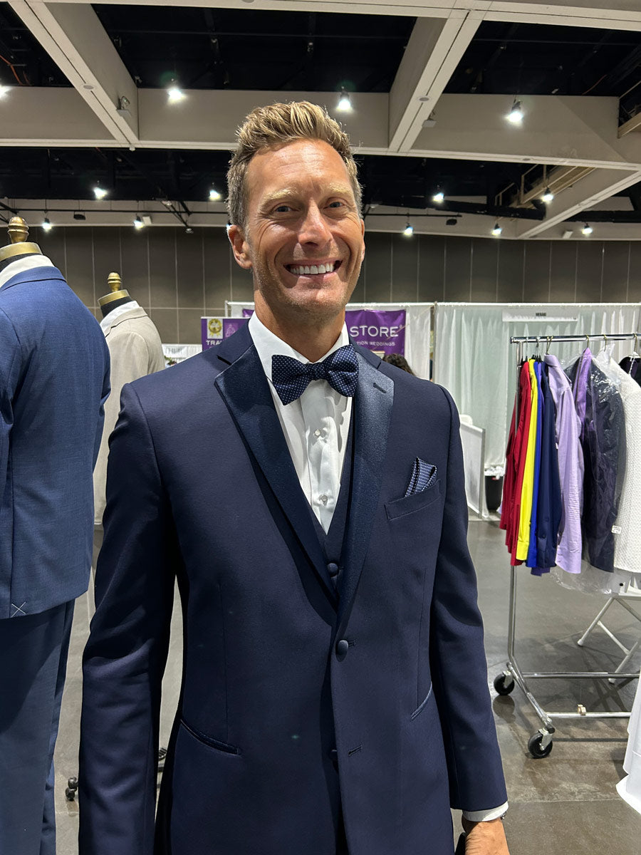 Close-up of a man wearing a navy blue tuxedo with blue lapel while at a bridal show.