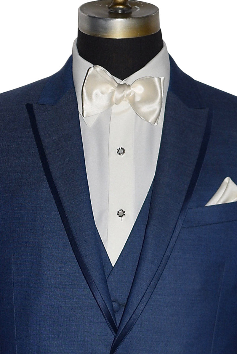 very close up of a mannequin wearing a  new blue peak lapel tuxedo with ivory "tie-yourself" bowtie and ivory shirt with pearl studs and cufflinks against a white background
