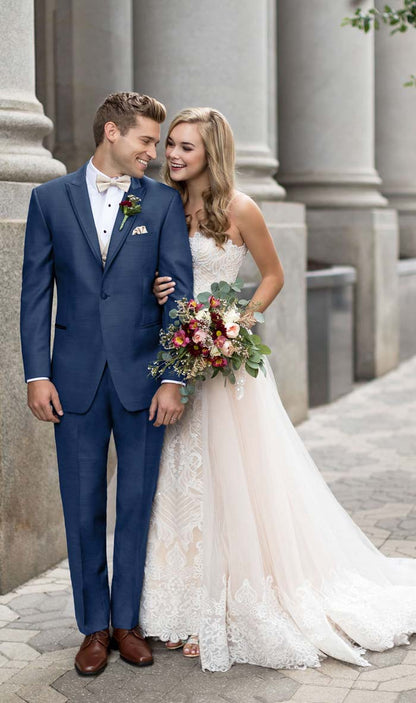 Man in a new-blue 3-piece tuxedo and woman in a white wedding dress standing together outdoors.