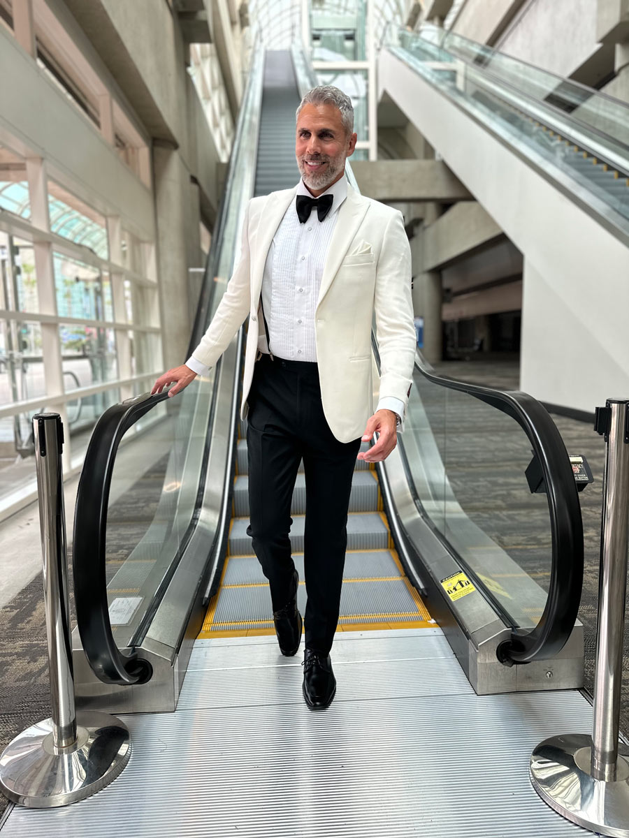 man wearing an ivory peak lapel dinner jacket with texture coming down an escalator  