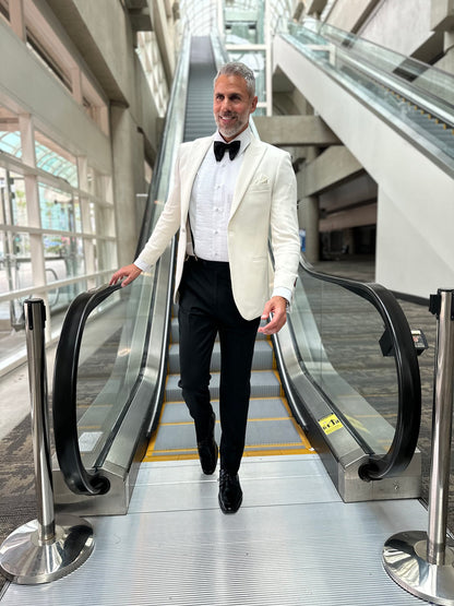man wearing an ivory peak lapel dinner jacket with texture coming down an escalator  