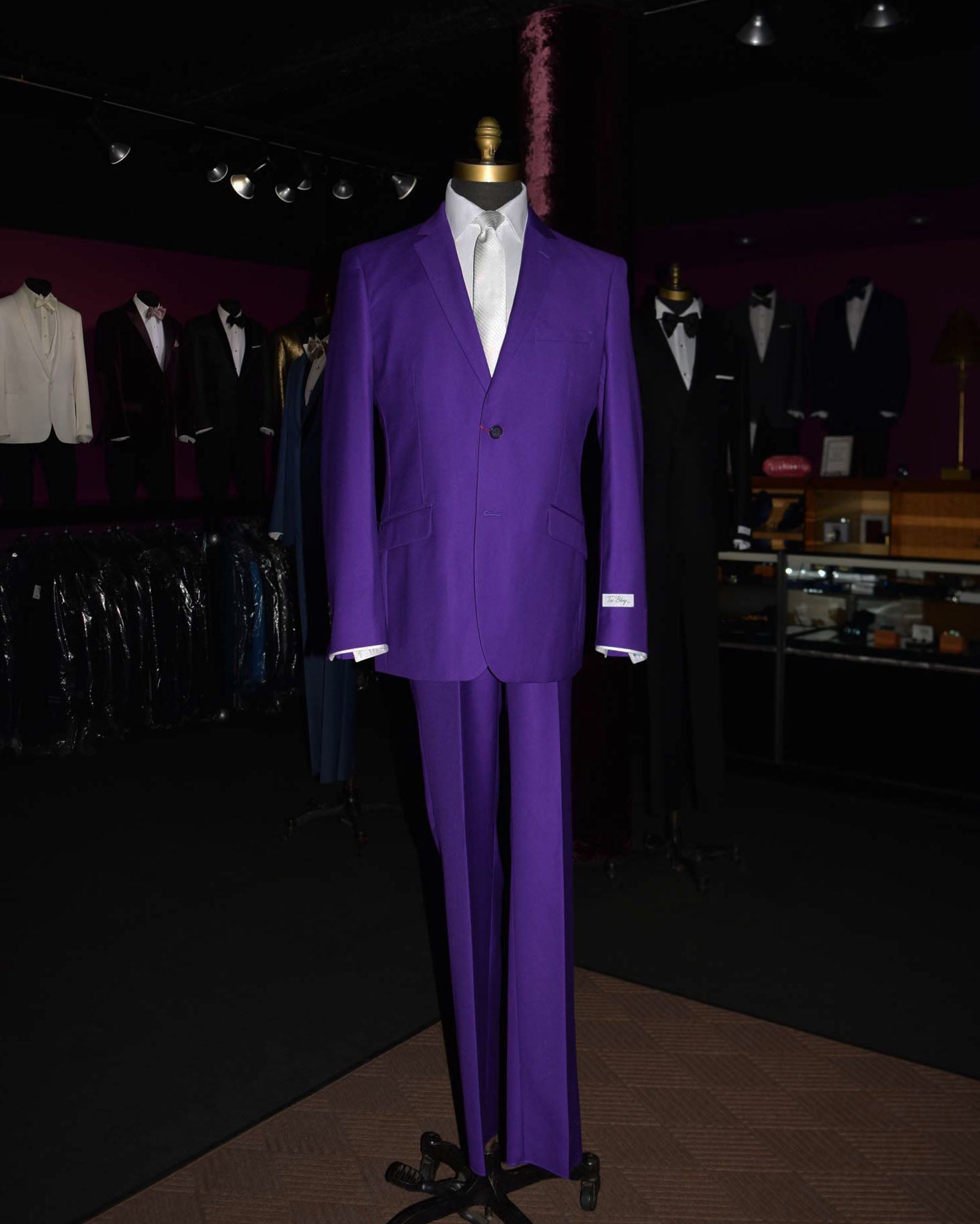 Purple suit with long white dress tie on a mannequin in a mens suit store with other suits in the background.