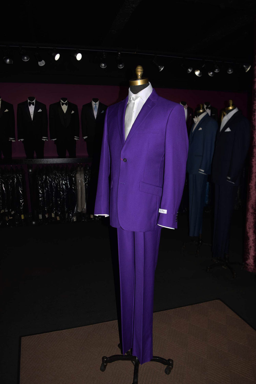 mannequin wearing a men's purple suit inside a high-end mens store with other suits on display