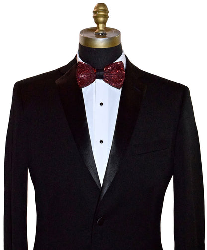 Black tuxedo with a white shirt and red sequin bow tie on a mannequin against a white background.