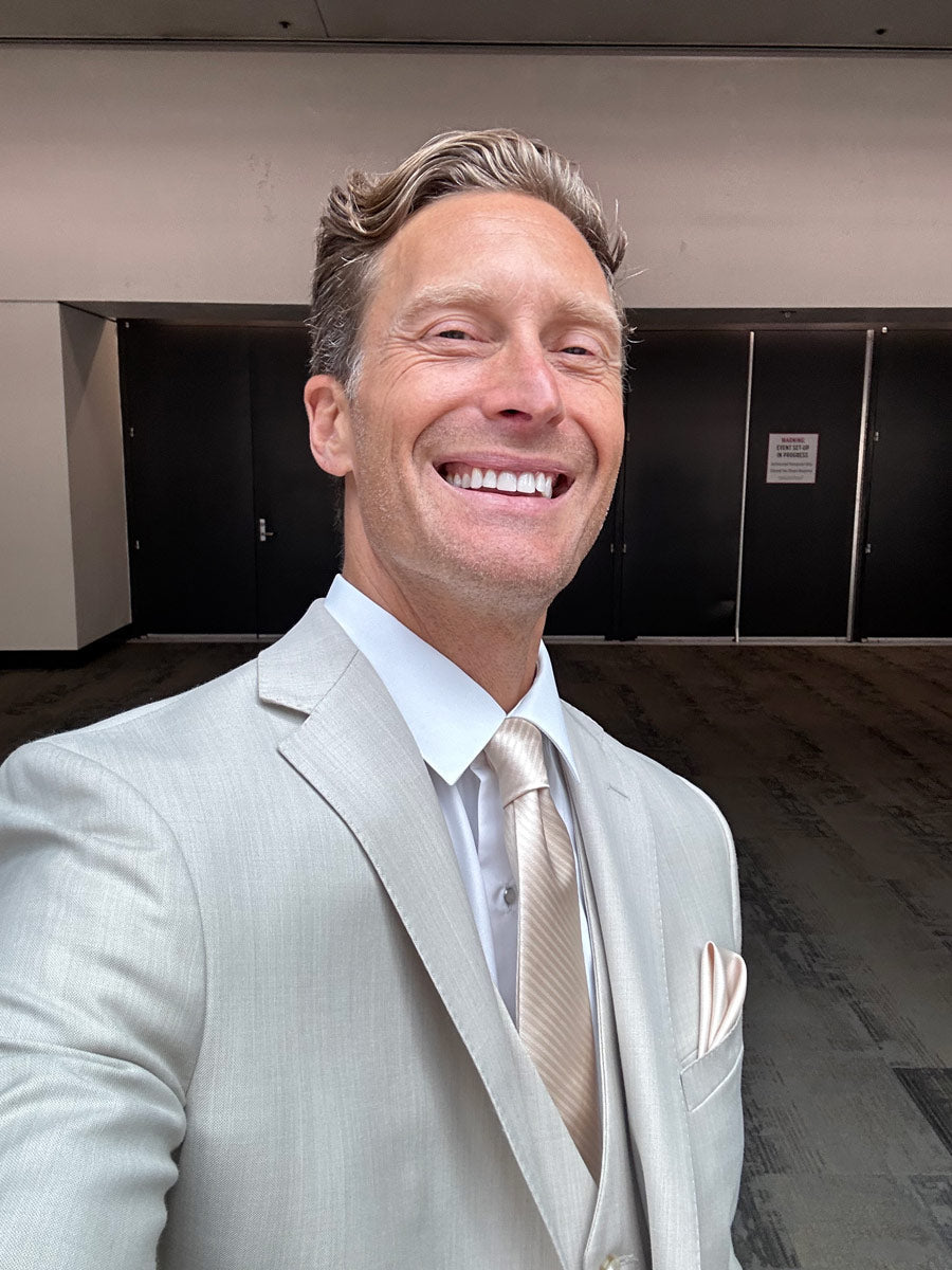 Model wearing a light tan fitted suit at a banquet hall.