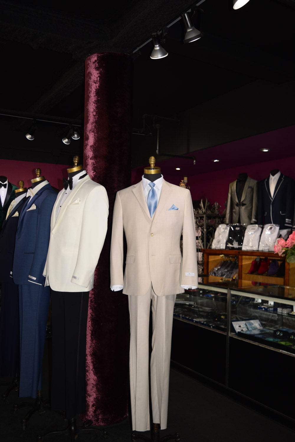 life size mannequin wearing a tan suit with a baby blue dress tie inside a tuxedo shop with mannequins in the background