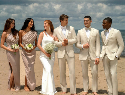 Photo of groom and groomsmen wearing tan slim fit suit while on the beach with the ocean in the background. 