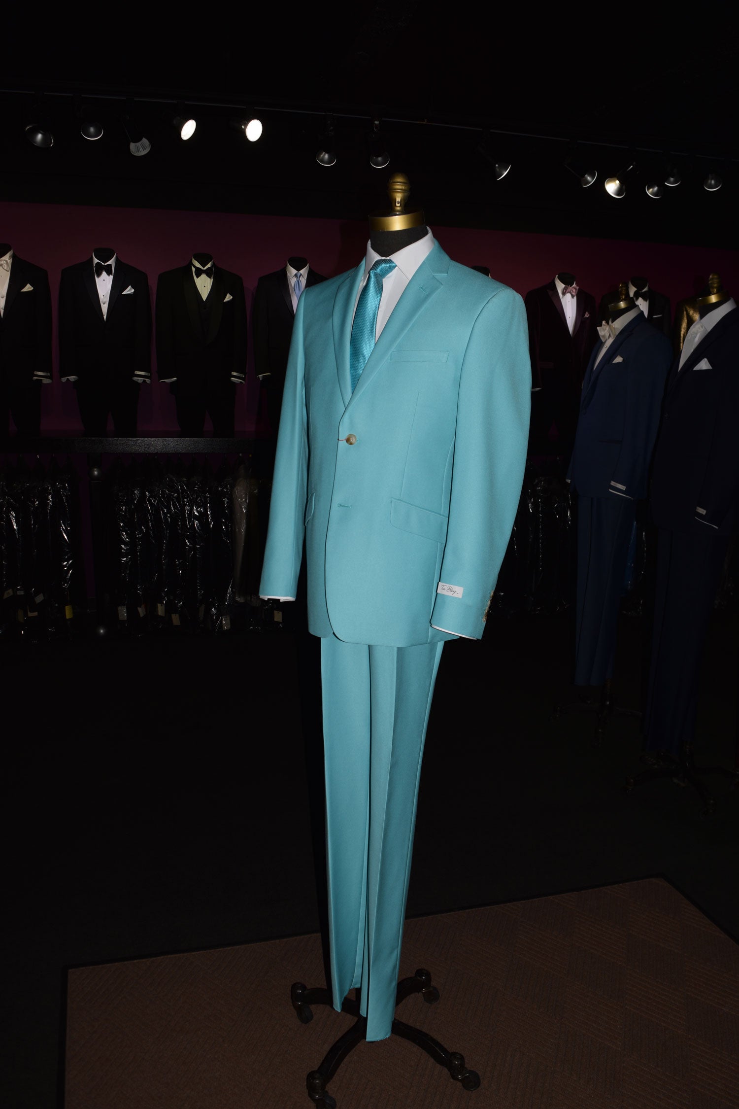 Mannequin wearing a tiffany blue suit with tiffany blue dress tie inside  mens store with other suits on display