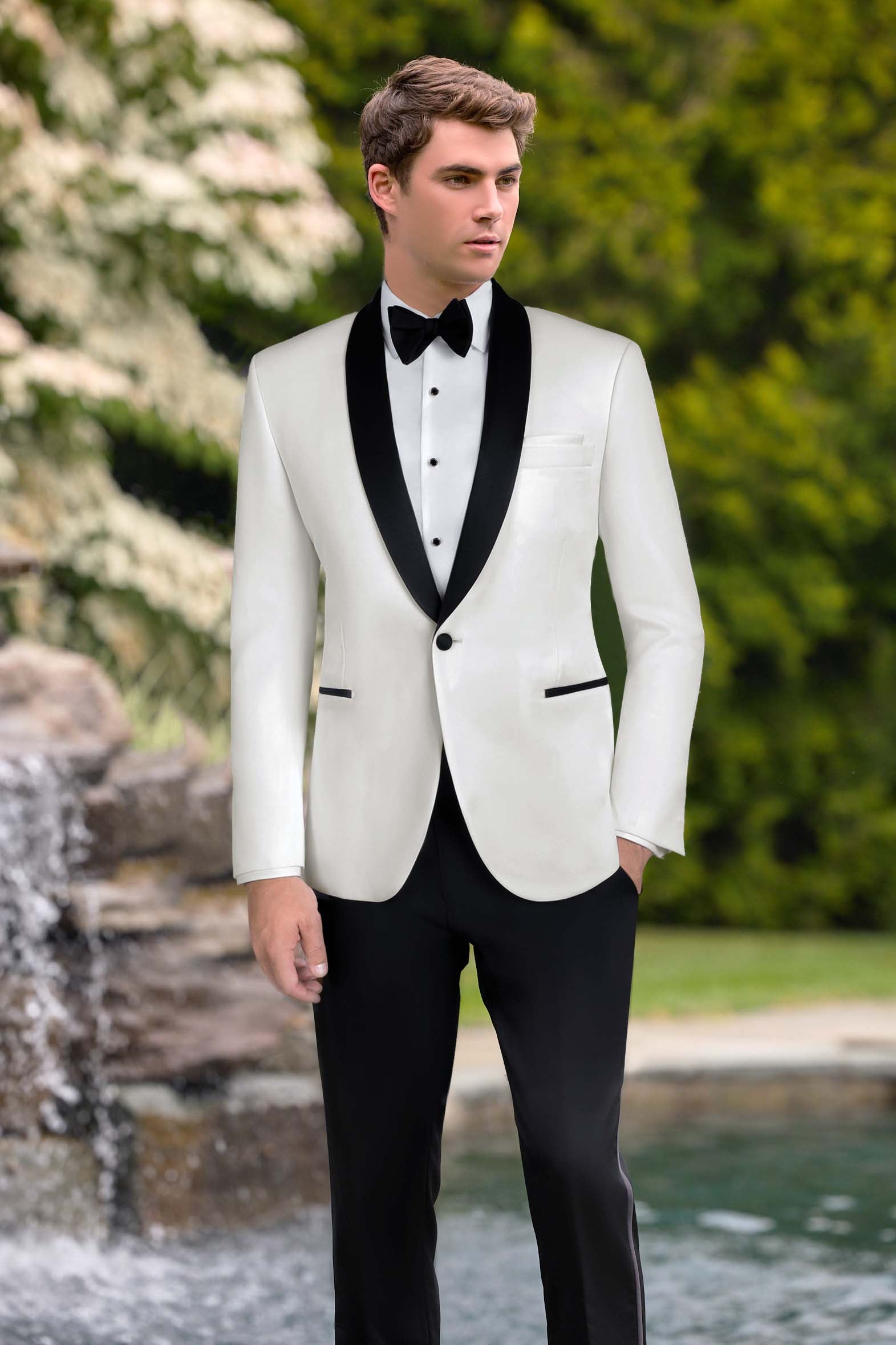 Handsome man wearing an ivory tuxedo with black lapels outside near a fountain.