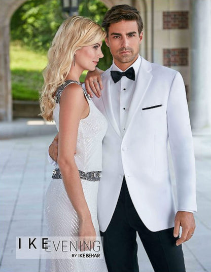 Man in a white notch lapel tuxedo and woman in a white evening gown standing together outdoors.