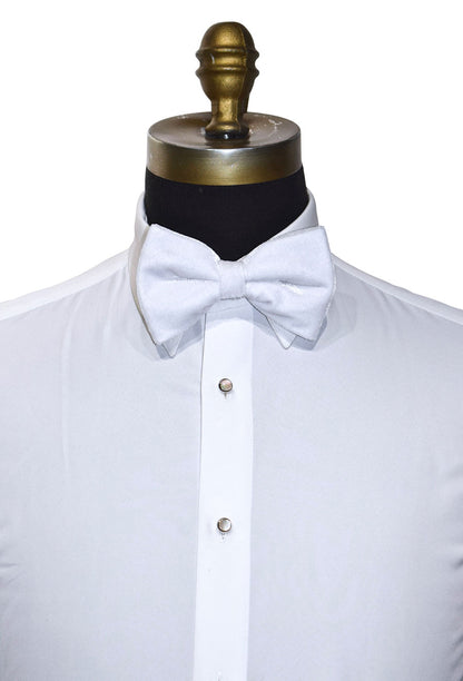 White velvet bow tie on a white dress shirt with a mannequin in front of a white background